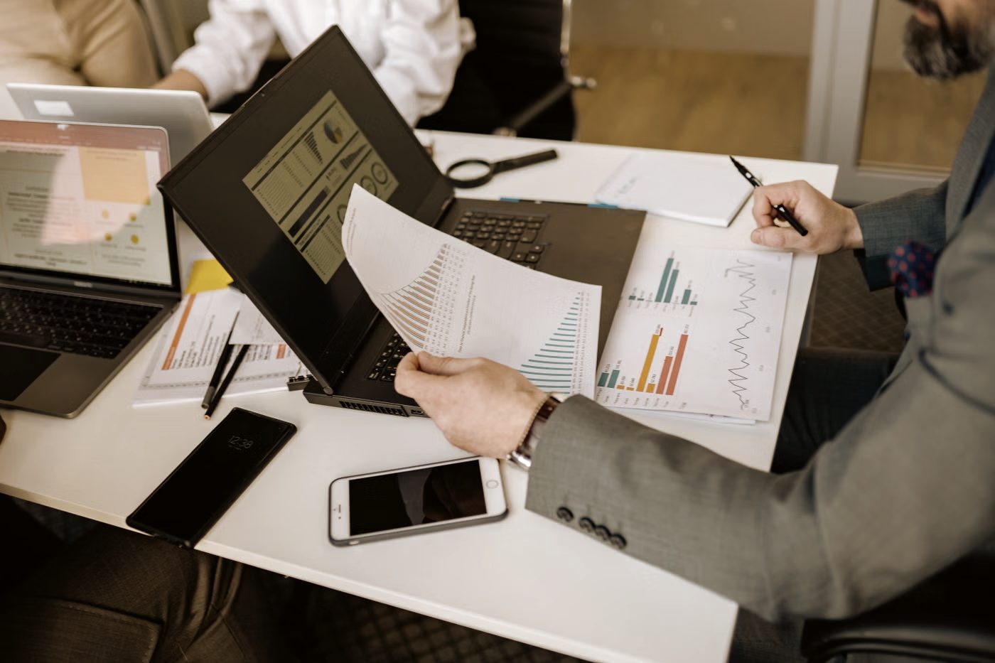 Printed reports and charts spread across a desk beside a laptop