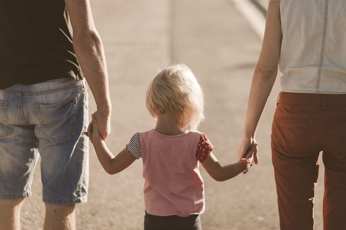 Two parents walking while holding a young child's hands